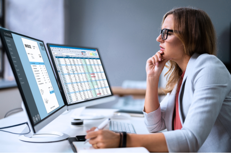 Accountant reviewing an invoice and spreadsheet on dual monitors in an accounting firm office